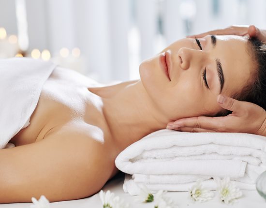 Beautician massaging face of young woman relaxing on fresh soft towels in beauty salon